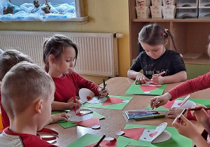 Dzieci przyklejają na kartonach elementy św. Mikołaja.